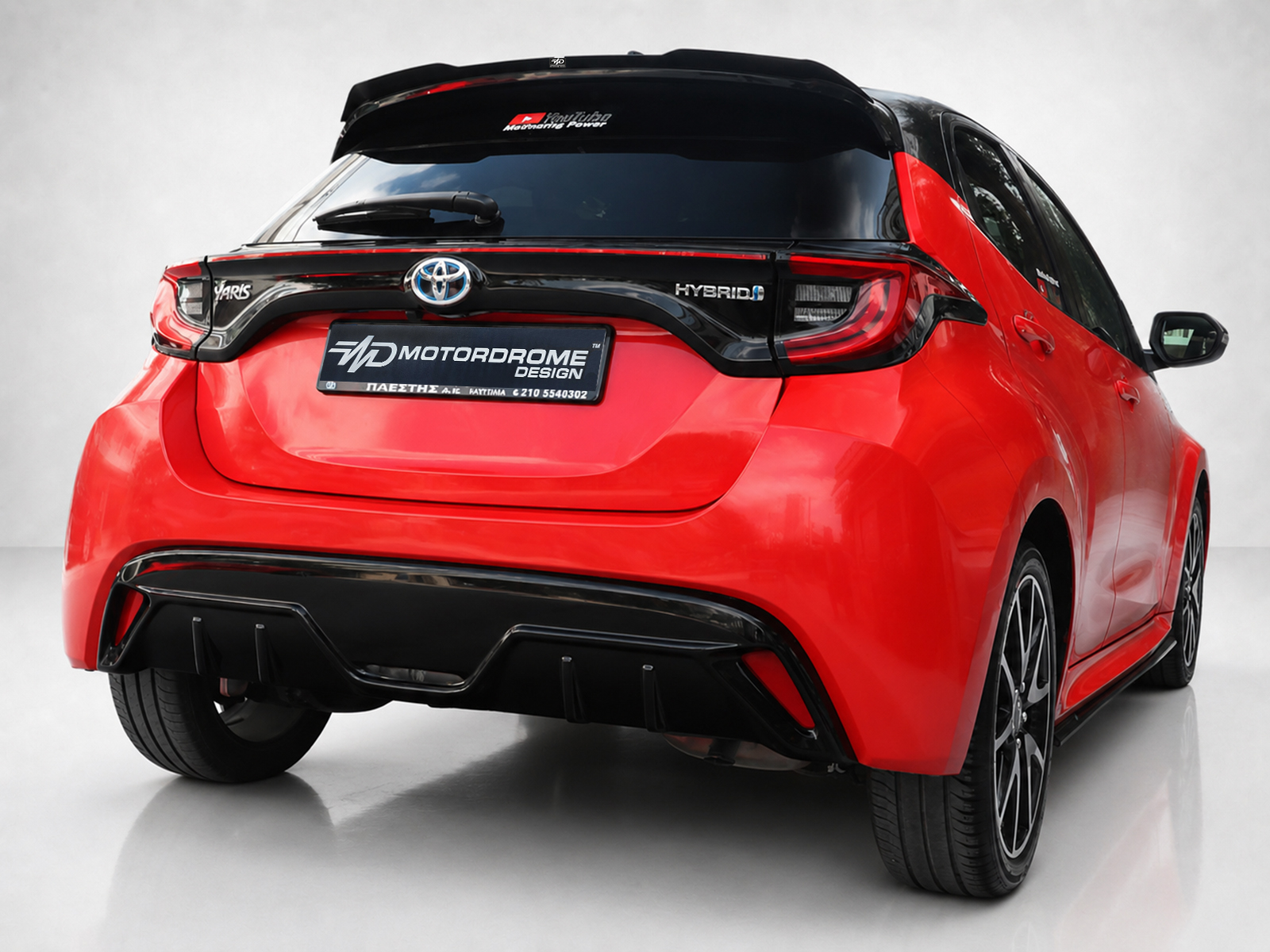 K169-003_1jpg - OPSHOLDERS Rear view of a red Toyota Yaris Hybrid with a black spoiler and prominent taillights in a studio setting