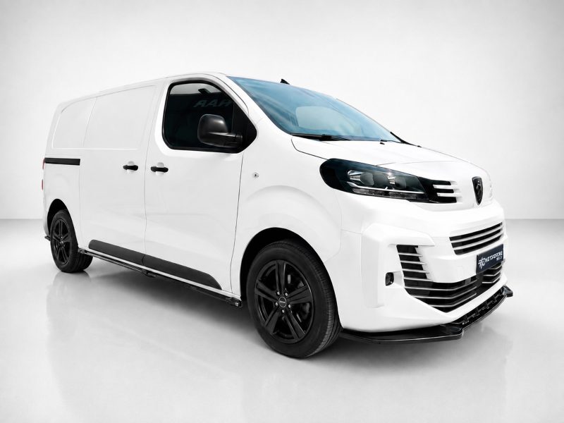 White cargo van with black wheels on a light gray studio floor, angled from the front-left side.