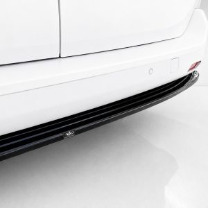Close-up of a white vehicle's side, featuring a black running board and small chrome emblem near the bottom edge