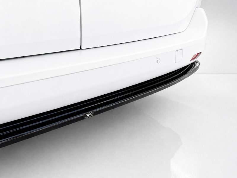 Close-up of a white vehicle's side, featuring a black running board and small chrome emblem near the bottom edge