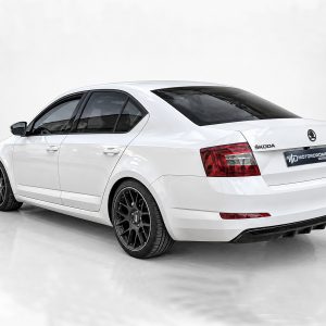 K171-001_2jpg - OPSHOLDERS White Škoda sedan shown from the rear-left angle in a studio, featuring black multi-spoke aftermarket wheels and red tail lights.