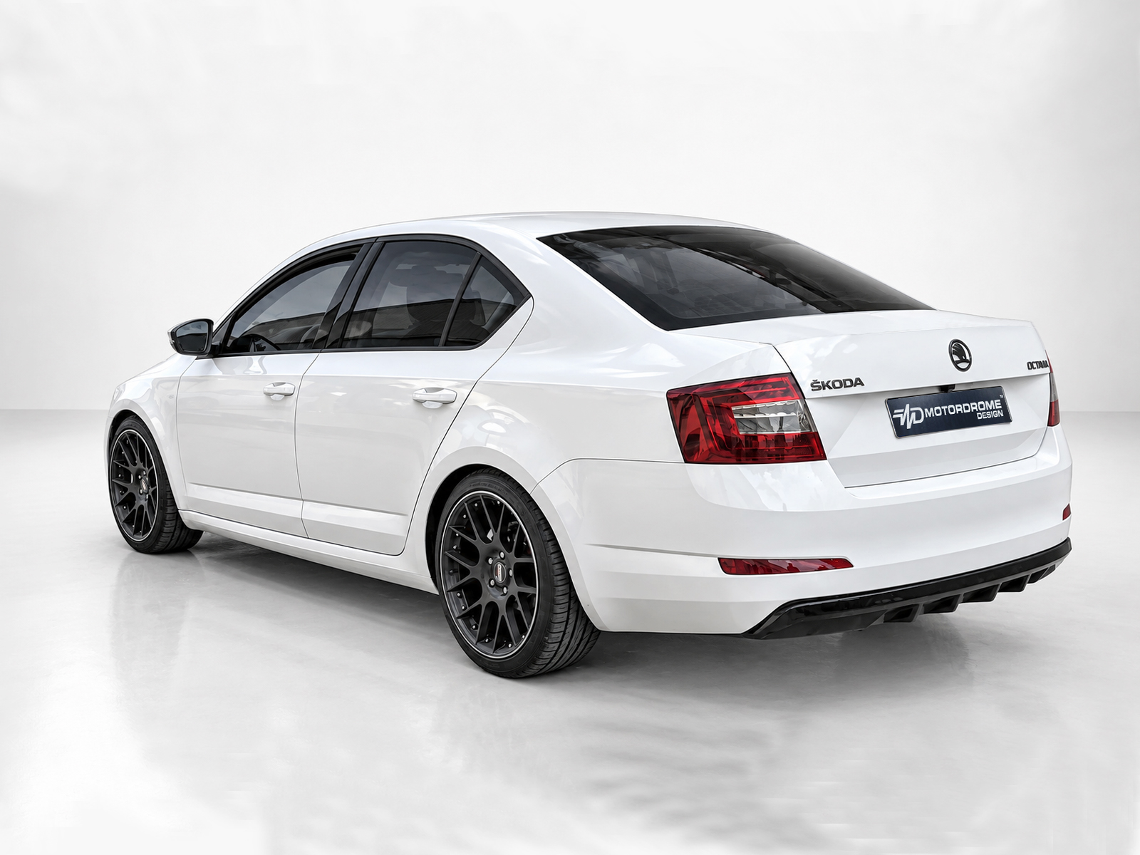 K171-001_2jpg - OPSHOLDERS White Škoda sedan shown from the rear-left angle in a studio, featuring black multi-spoke aftermarket wheels and red tail lights.