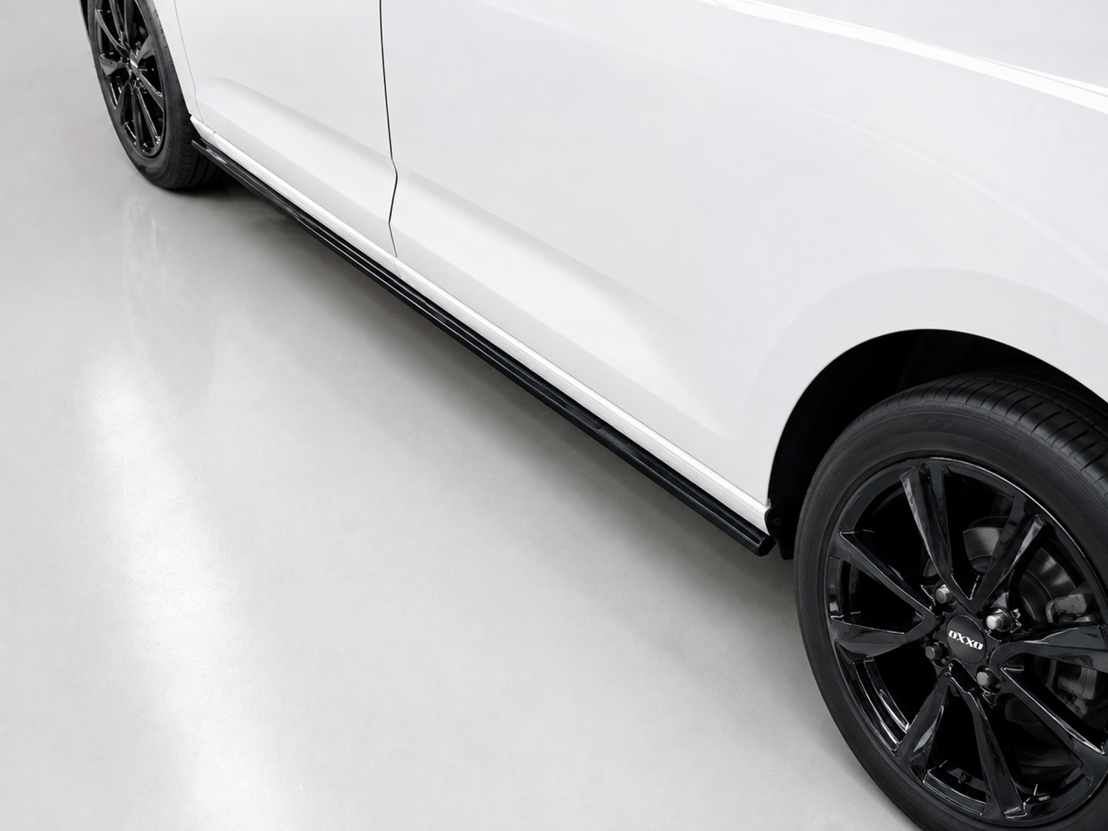K172-003_1jpg - OPSHOLDERS White car body with a black multi-spoke wheel shown from the side, focusing on the lower panel and tire on a light showroom floor.