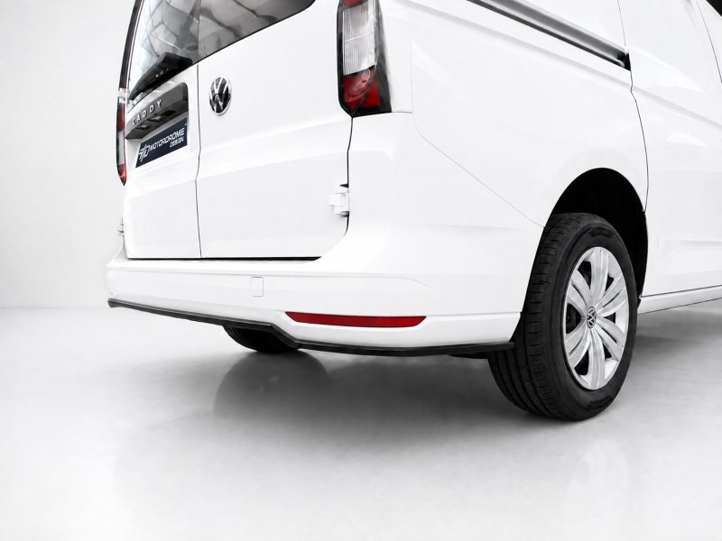 White VW van seen from the rear-right, showing taillight, bumper, and a visible wheel with the VW emblem.
