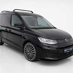 Black Volkswagen van shown in a studio setting, featuring a roof rack and large, intricate alloy wheels (front-quarter view).