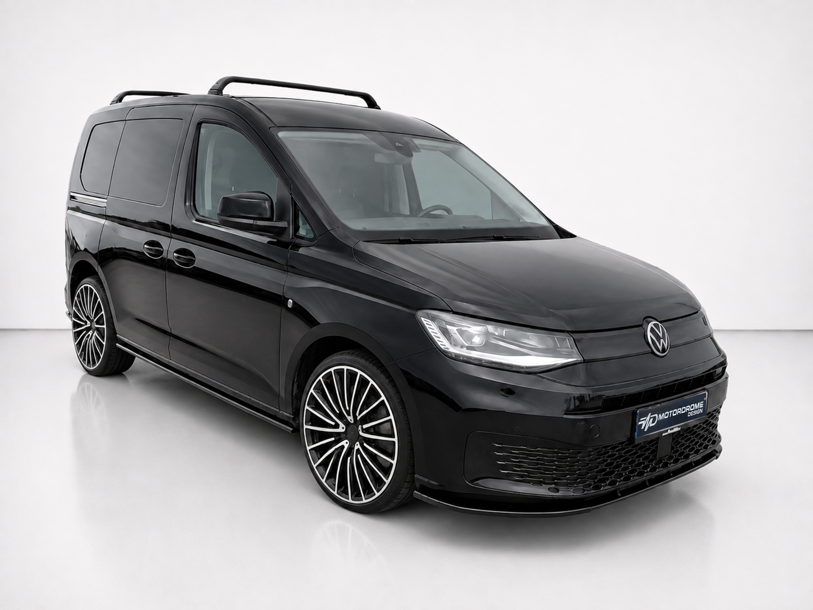 K172-005_1jpg - OPSHOLDERS Black Volkswagen van shown in a studio setting, featuring a roof rack and large, intricate alloy wheels (front-quarter view).