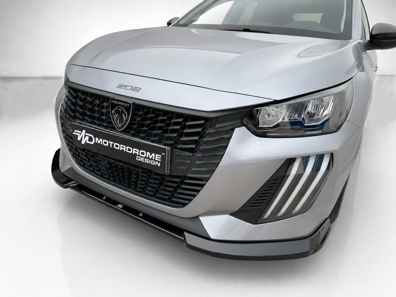 Front-angle view of a silver Peugeot car showing its large grille, badge, and LED headlight cluster with a MotorDrome Design plate on the bumper.