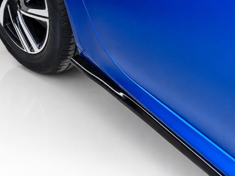 Close-up of a blue car's lower body panel, chrome trim, and a black side skirt beside the wheel.