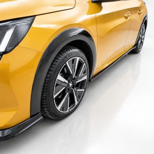 Close-up of a yellow car's front fender, headlight, and alloy wheel in a studio setting