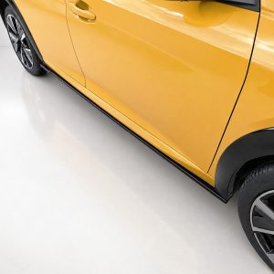 Side view of a yellow car with a black wheel and lower trim, shown indoors on a light showroom floor.