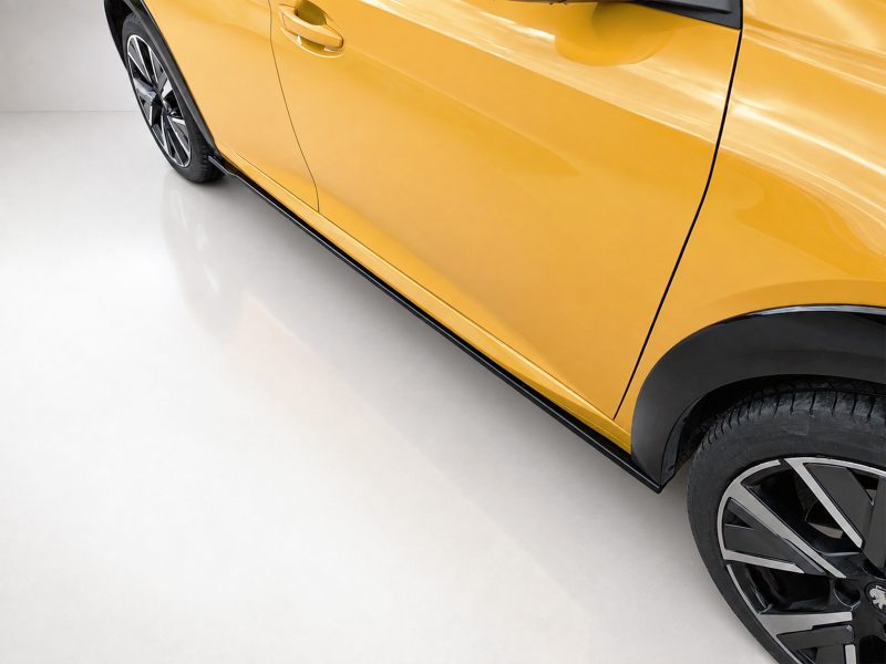 Side view of a yellow car with a black wheel and lower trim, shown indoors on a light showroom floor.