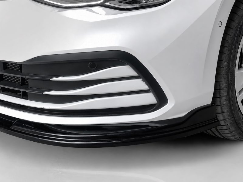 K174-001_3jpg - OPSHOLDERS Close-up of a white car's front bumper with black grille accents and a visible tire on the right edge.