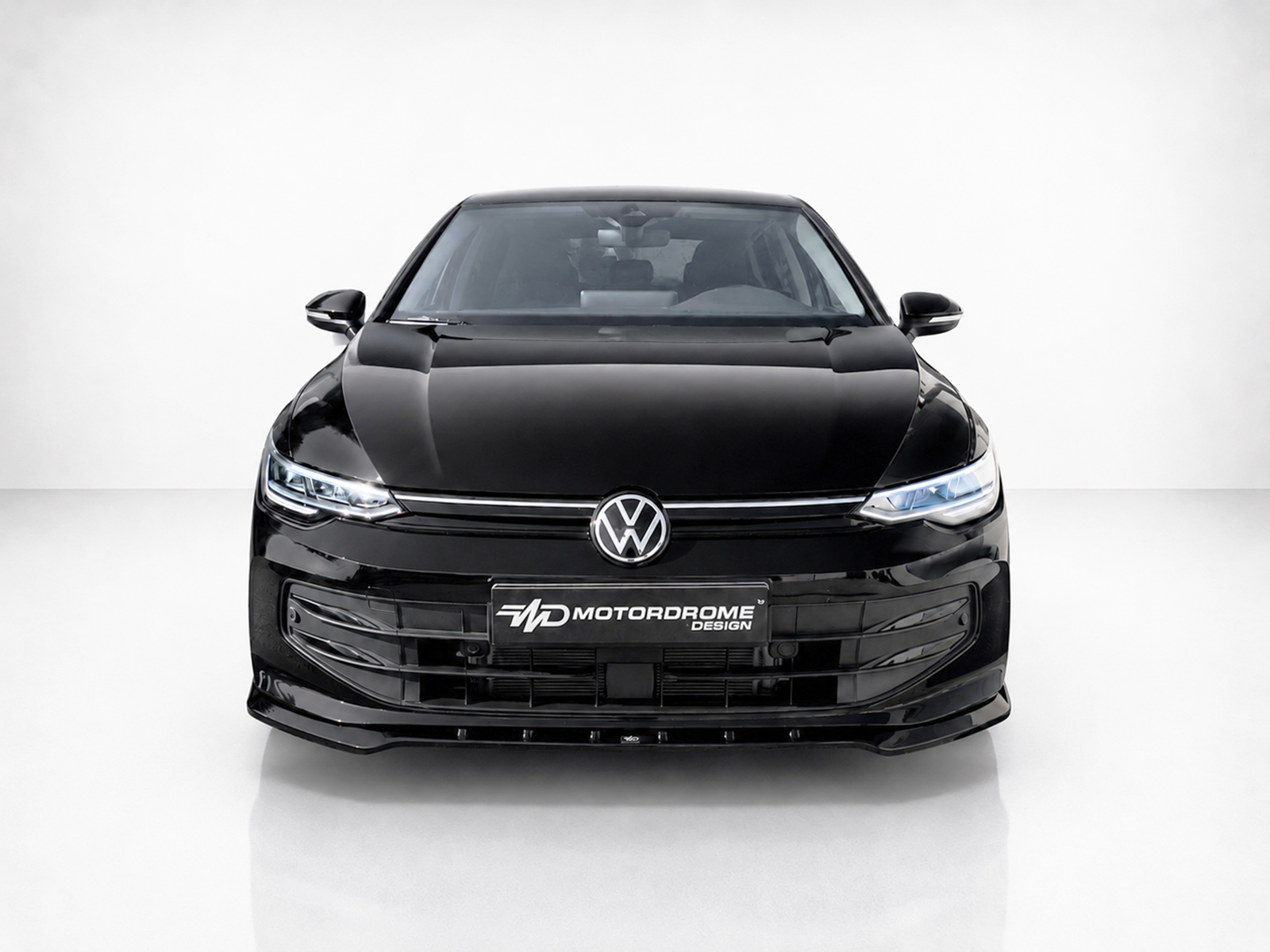K174-002_1jpg - OPSHOLDERS Front view of a glossy black Volkswagen car in a bright studio, logo and Motordrome Design plate visible on the grille area