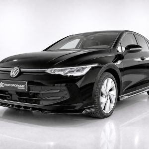 K174-002_2jpg - OPSHOLDERS Front three-quarter view of a sleek black Volkswagen sedan in a studio setting, chrome grille and VW emblem visible on the grille.