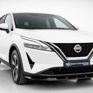 White Nissan SUV shown from a three-quarter front view, highlighting the bold grille and sleek headlights with a MotorDrome Design plate in front