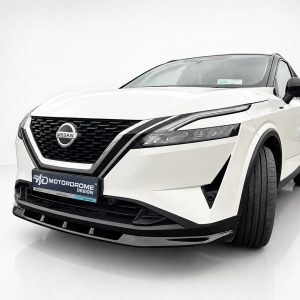 Front-left angled view of a white Nissan vehicle in a studio, showcasing the bold V-motion grille and sharp headlights.