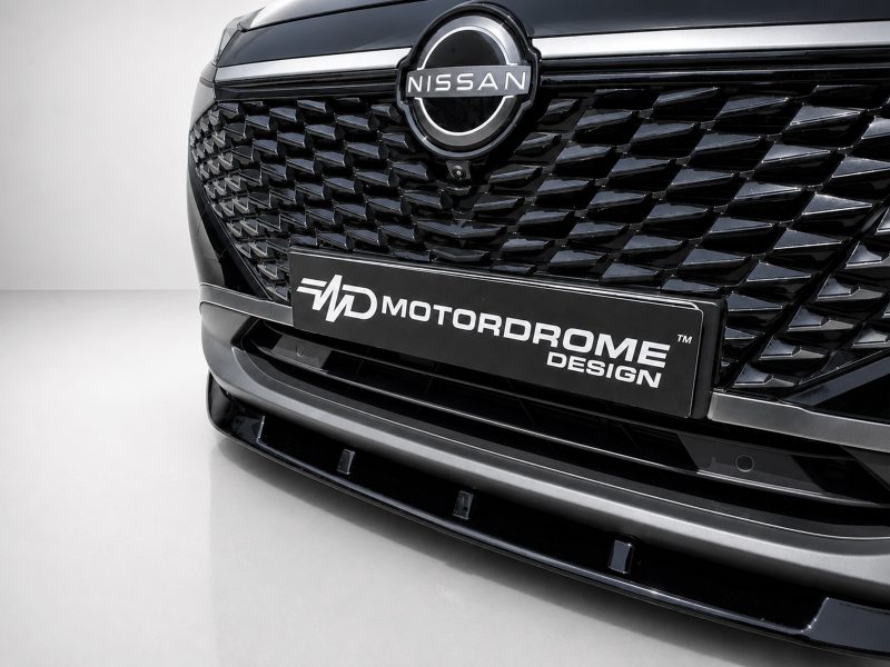 Close-up of a Nissan emblem on a glossy black grille with a diamond-patterned design and a Motordrome Design license plate.