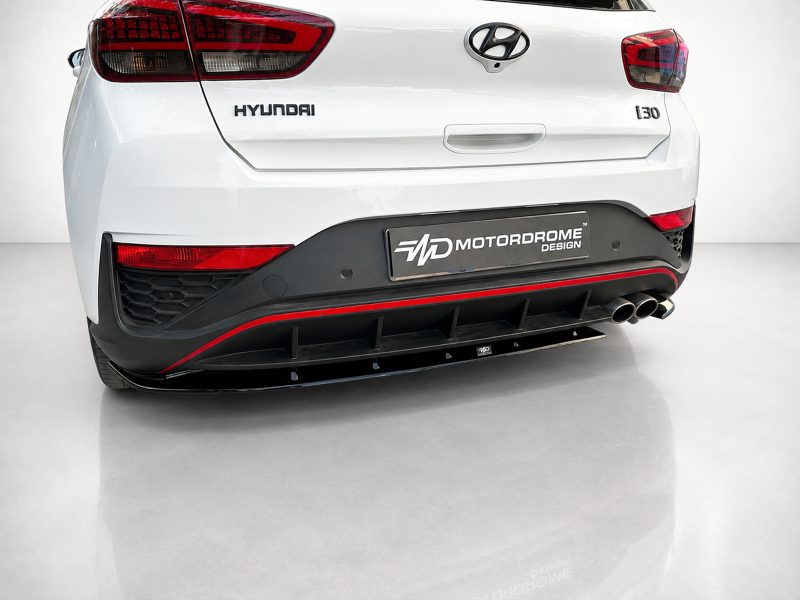 K180-002_4jpg - OPSHOLDERS Rear view of a white Hyundai hatchback showing taillights, Hyundai badge, and a MotorDrome Design plate on the bumper with a black diffuser and red trim.