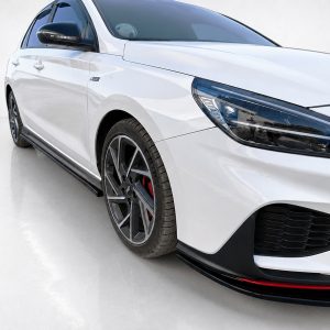 White sports car photographed from a front-left angle, showing the headlight, front bumper, and alloy wheel with red brake calipers