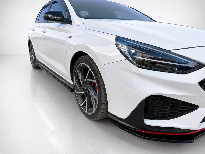 White sports car photographed from a front-left angle, showing the headlight, front bumper, and alloy wheel with red brake calipers