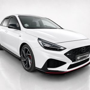 Front three-quarter view of a white Hyundai sporty hatchback with black mesh grille, large dark alloy wheels, and red brake calipers in a studio setting