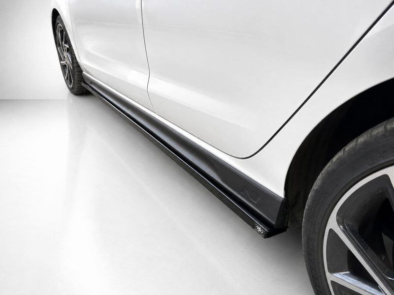 White car side view showing a black side skirt and alloy wheel at the rear area