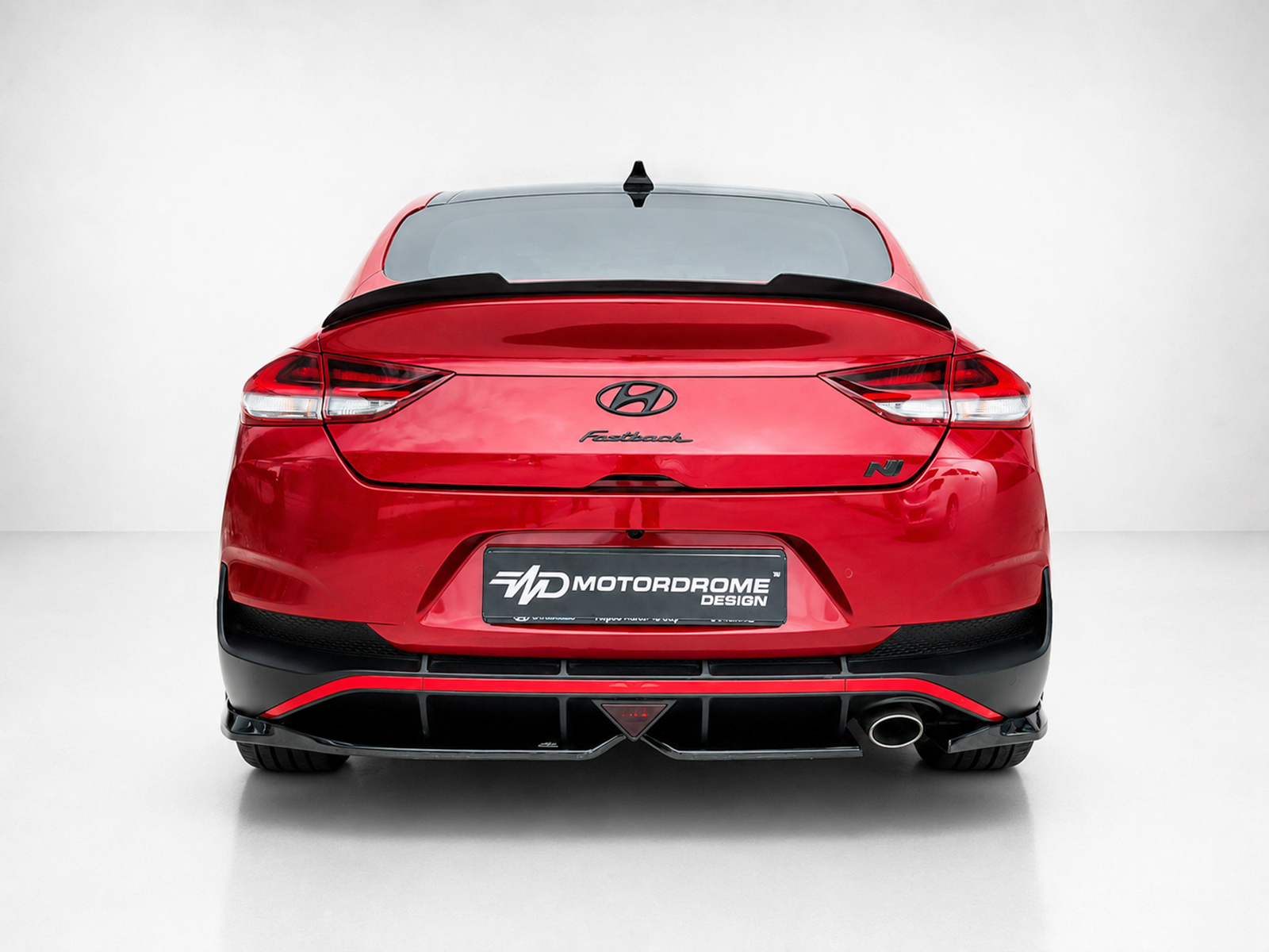 K180-005_1jpg - OPSHOLDERS Rear view of a red Hyundai Fastback in a studio setting, showing taillights, spoiler, and a Motordrome Design plate.