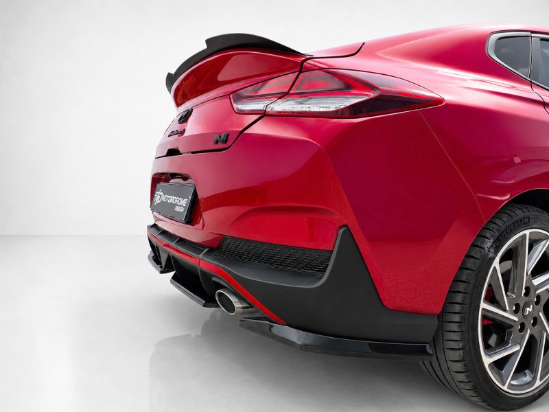 K180-005_3jpg - OPSHOLDERS Rear three-quarter view of a glossy red sports car showing the taillight, exhaust, and wide rear wheel in a showroom setting.