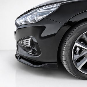 Close-up of a black car's front left corner showing the headlight, fog light area, and alloy wheel in a studio setting.