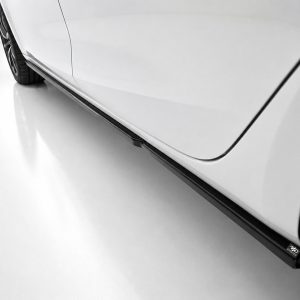 Close-up of a white car's side with a black side skirt and part of the rear wheel visible on a reflective floor.
