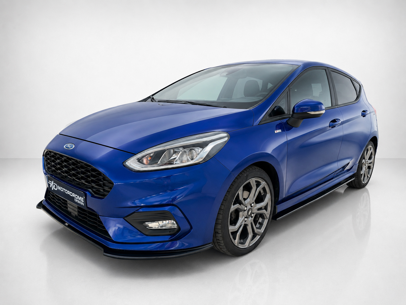 K182-005_1jpg - OPSHOLDERS Blue Ford hatchback photographed from a left-front angle in a clean studio, showing the grille and alloy wheels in detail.