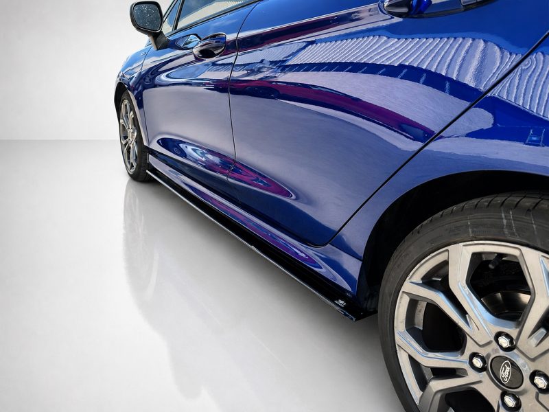 K182-005_4jpg - OPSHOLDERS Close-up of a blue car's side, showing the door, glossy paint, and front wheel rim.