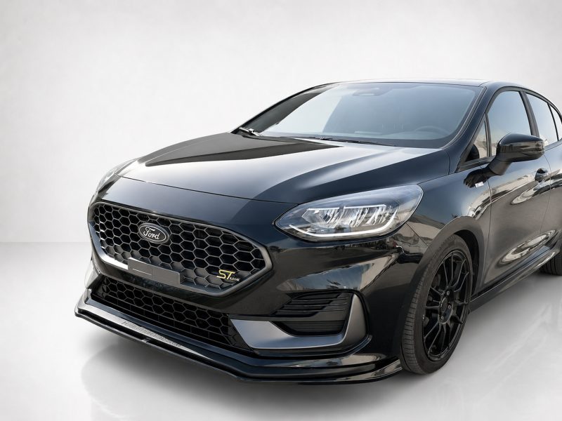 Front three-quarter view of a glossy black Ford car, showing honeycomb grille, prominent headlights, and side mirrors.