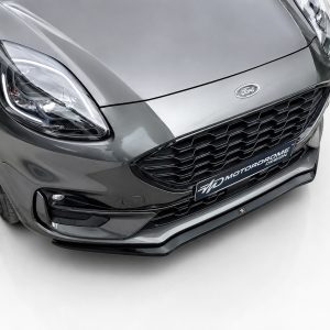 Front close-up of a gray Ford car showing headlight, grille, and badge in a studio setting.