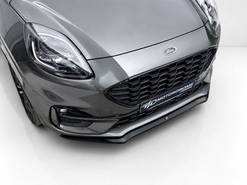 Front close-up of a gray Ford car showing headlight, grille, and badge in a studio setting.