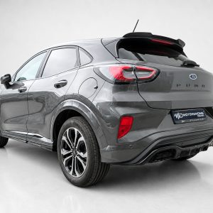 Gray Ford Puma compact SUV viewed from rear three-quarters in a studio setting. It features distinctive red taillights and alloy wheels.