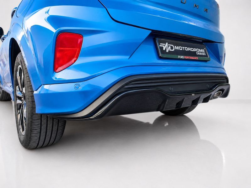 Rear view of a bright blue SUV showing the left taillight, bumper, and license plate area with a car design logo plate.