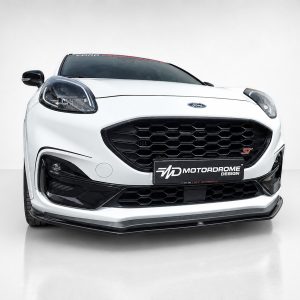 Front view of a white Ford car with a large black honeycomb grille and ST badge in a studio setting, Motordrome Design plate visible on the bumper.