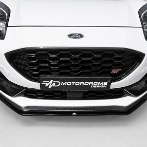 Front view of a white Ford car showing a large black honeycomb grille and Ford badge with a Motordrome Design plate above the bumper edge.