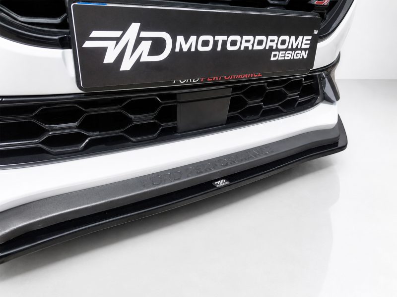 Front bumper close-up of a white Ford with a honeycomb grille and a Ford Performance lip plate reading 'FORD PERFORMANCE' (car show/photo set).
