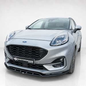 Front-left view of a silver Ford car with a black honeycomb grille, minimalist studio background, and Motordrome Design plate visible on the bumper.