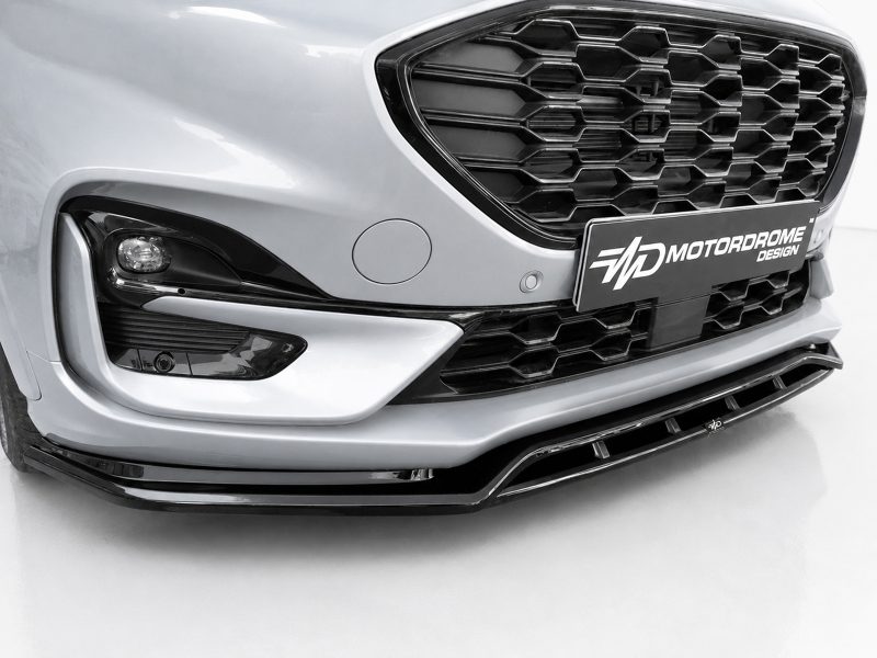 Close-up of a silver car's front end with a honeycomb grille, left headlight, and a MOTORDROME DESIGN license plate caping the front bumper.