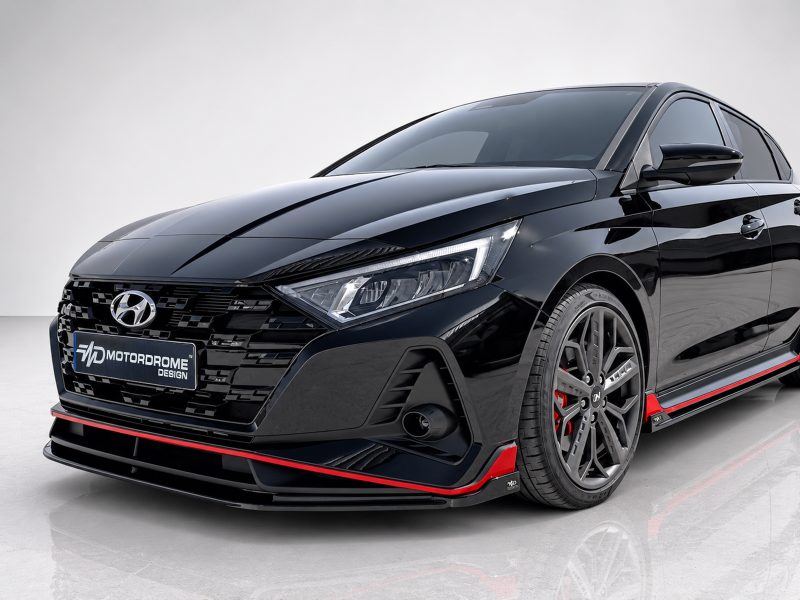 Black sports sedan, close-up front-left angle showing sleek grille, angular headlights, and red accent trim along the bumper and side skirts.