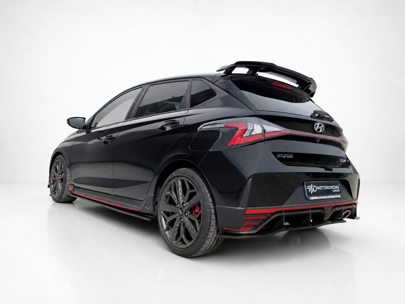 Black Hyundai hatchback with red racing accents and a large rear spoiler photographed in a studio.