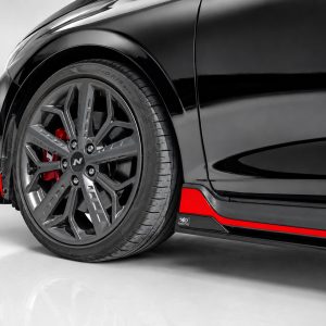 Close-up of a black car's front wheel with a silver multi‑spoke rim and red brake caliper visible behind the tire.