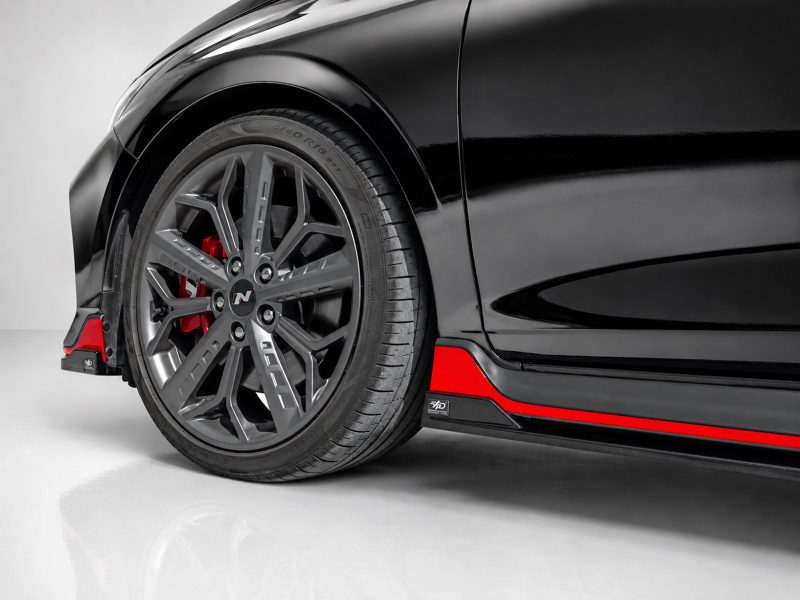 Close-up of a black car's front wheel with a silver multi‑spoke rim and red brake caliper visible behind the tire.