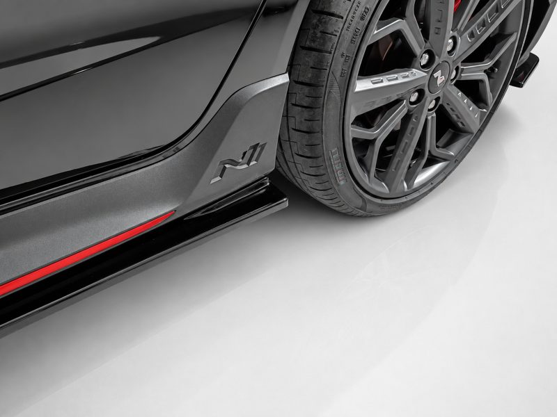 Close-up of a black sports car’s side panel and alloy wheel, with a red accent stripe along the rocker.
