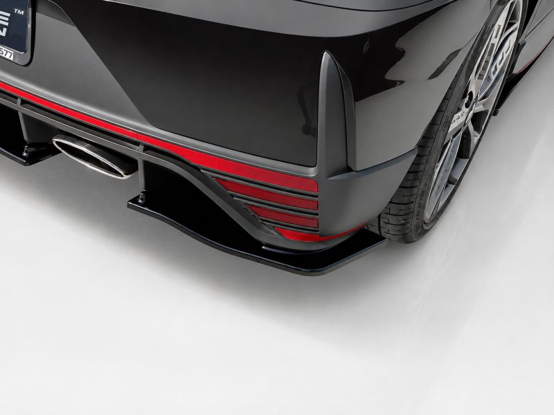 K185-003_5jpg - OPSHOLDERS Rear view of a black sports car with red trim, diffuser, and exposed exhaust tip in the lower bumper area, near a wheel.