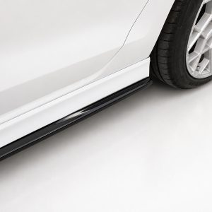 Close-up of a white car's side panel with a black running board and a silver multi-spoke alloy wheel visible at the rear/foreground.