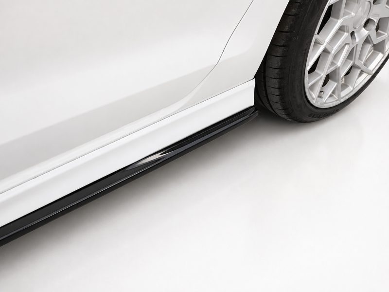 Close-up of a white car's side panel with a black running board and a silver multi-spoke alloy wheel visible at the rear/foreground.